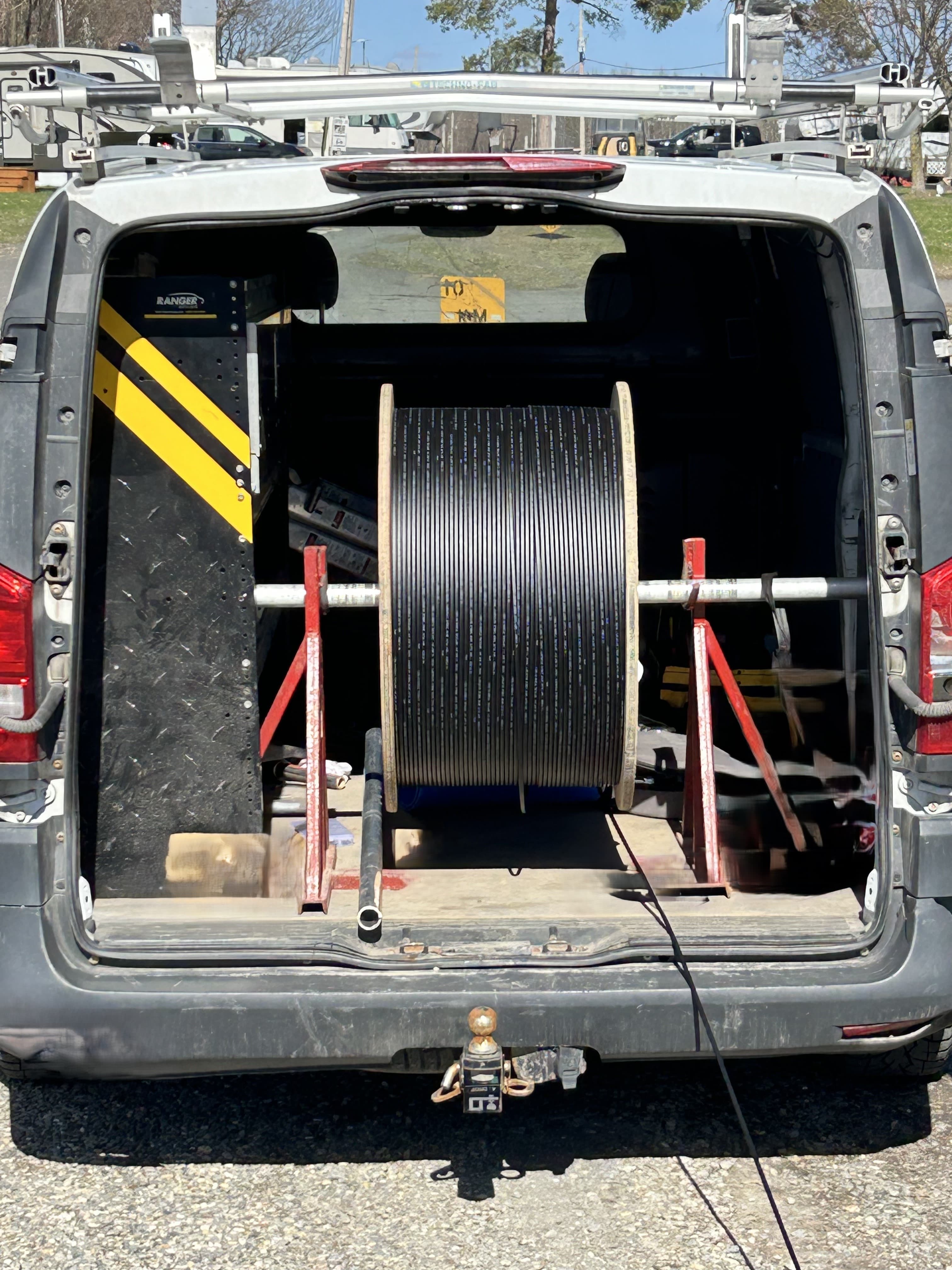 Large spool of black cable mounted on a red stand inside a white service van.